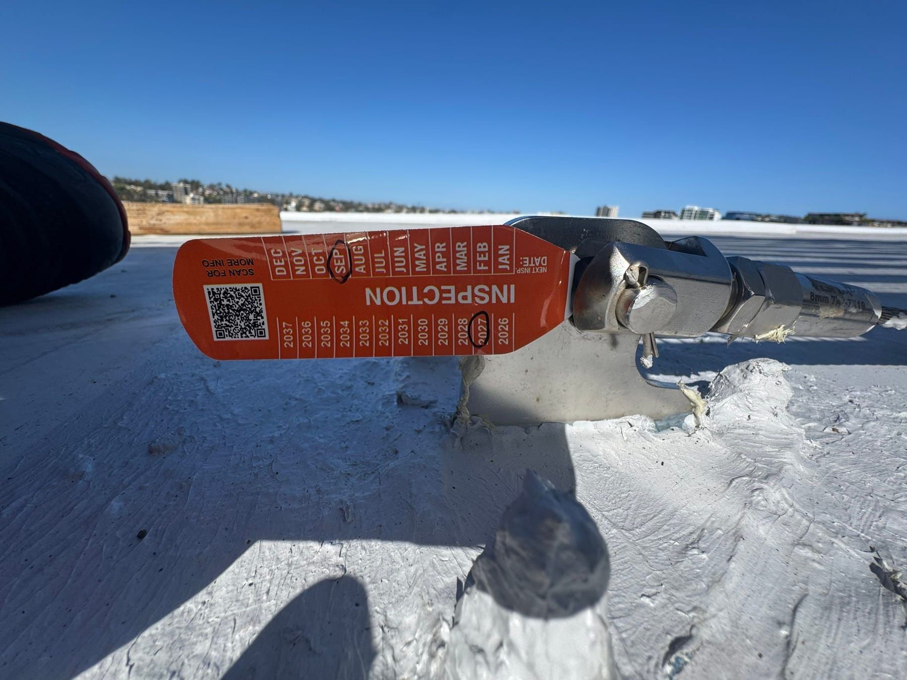 Inspection tag on a rooftop anchor point with a QR code and year markers
